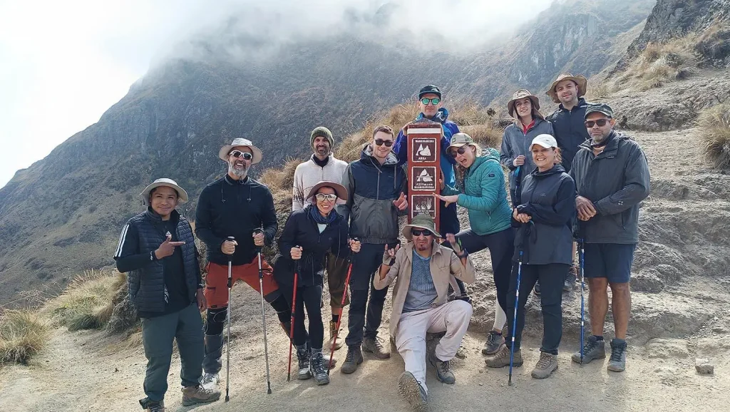 Grupo de senderistas celebra en el paso de montaña del Camino Inca, rodeado de neblina.
