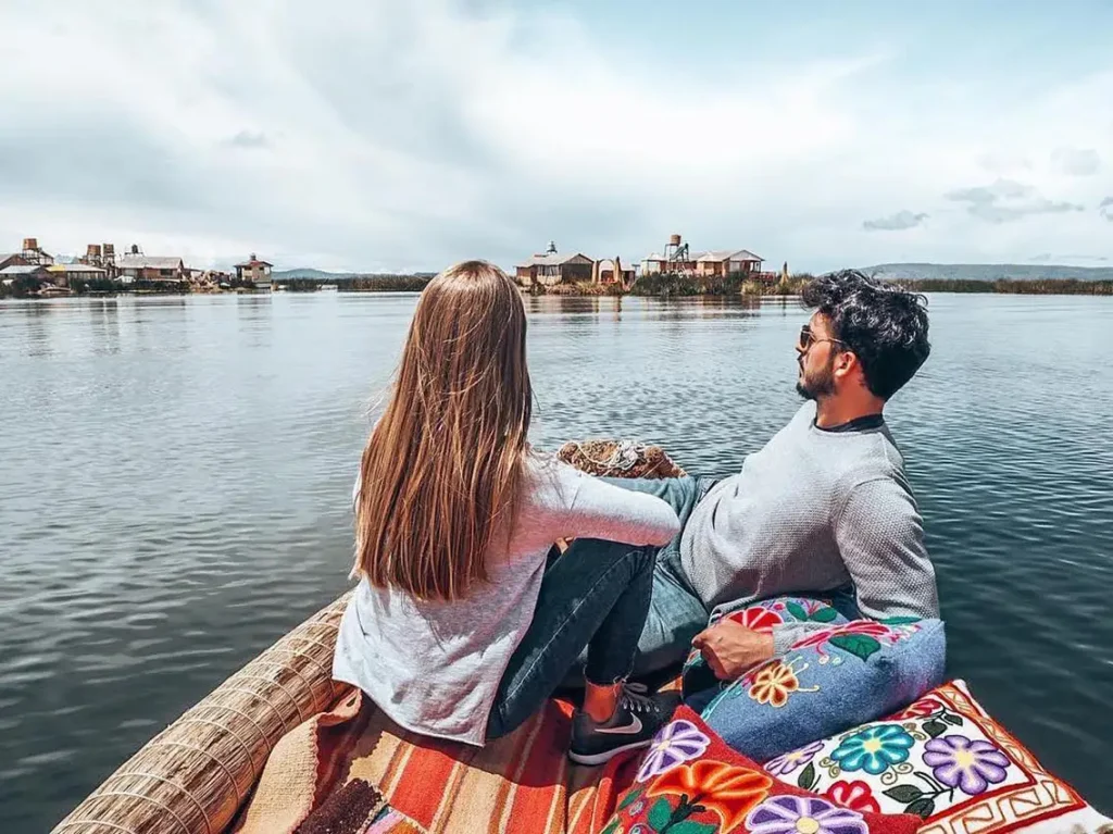 Pareja sentada en barca de totora mirando islas del lago Titicaca.