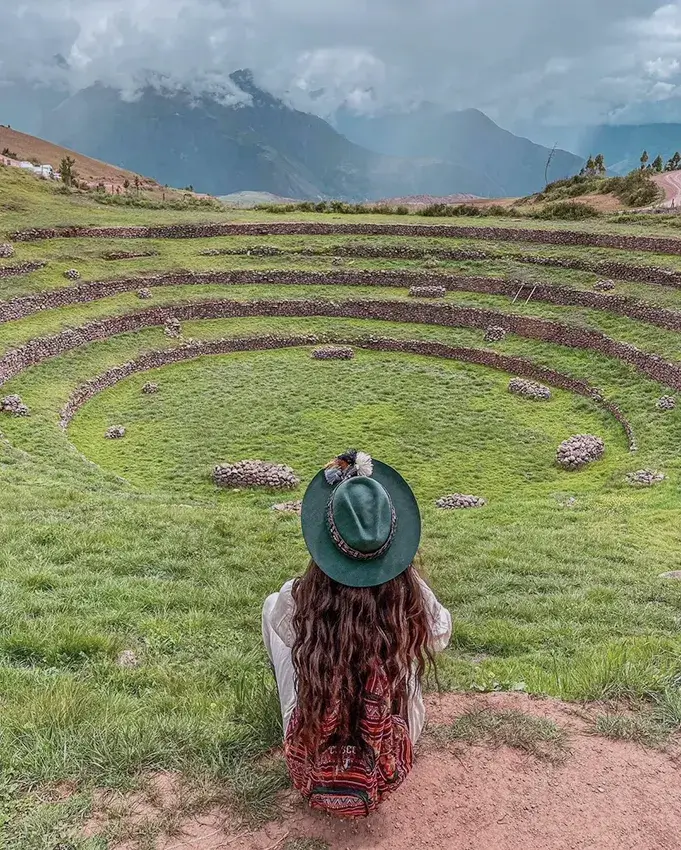 Turista disfrutando de las terrazas circulares de Moray en un valle verde.