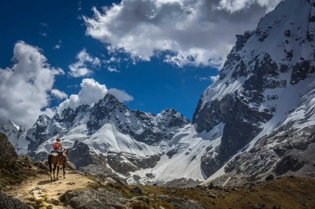 Persona a caballo en un sendero andino, con imponentes montañas nevadas del Salkantay al fondo.