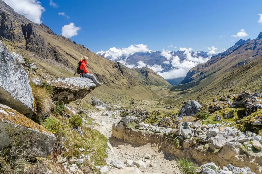 Mujer sentada en roca contempla el paisaje montañoso en la ruta Salkantay, Perú.
