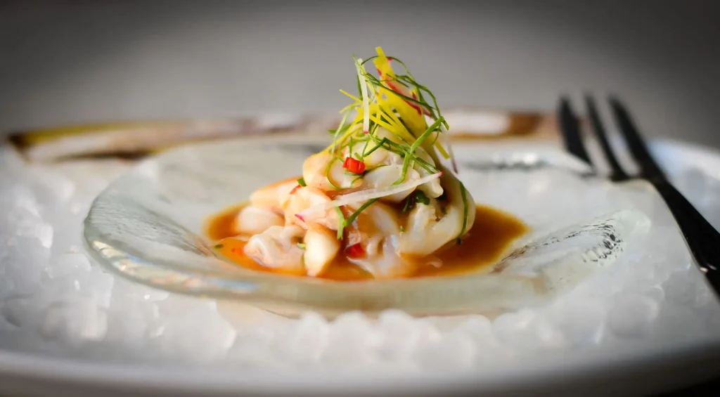Ceviche servido en plato de vidrio con jugo y hierbas frescas