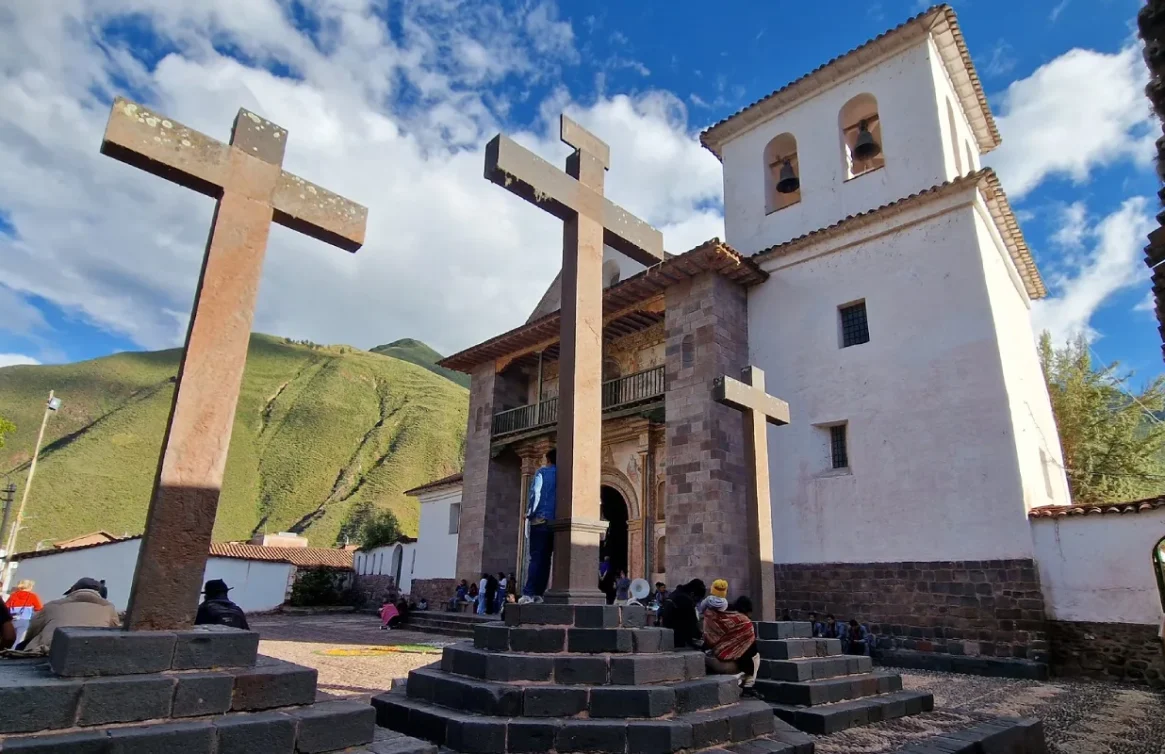 Iglesia de Andahuaylillas con cruces de piedra y montañas verdes.