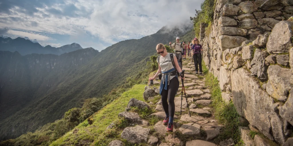 Turistas recorren el Camino Inca rodeados de montañas y antiguos muros de piedra.