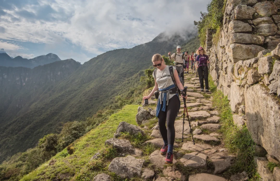 Turistas recorren el Camino Inca rodeados de montañas y antiguos muros de piedra.