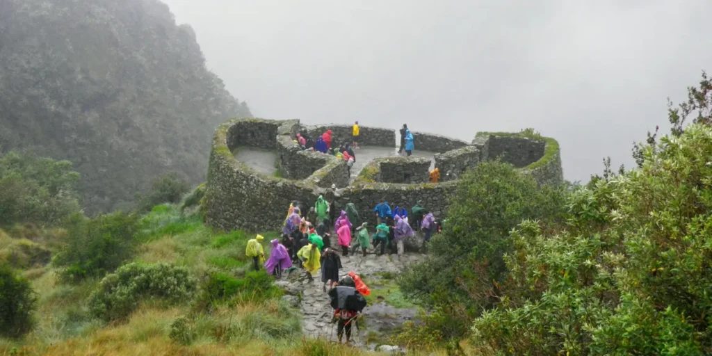 Caminantes con ponchos de lluvia en las ruinas semicirculares de Runkurakay, Camino Inca a Machu Picchu, Cusco, entre neblina