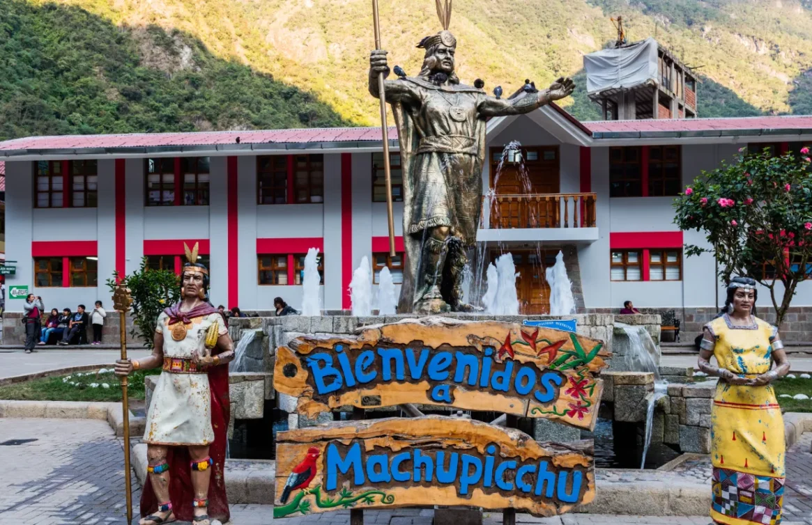 Escultura de un inca y cartel de bienvenida en la plaza principal de Aguas Calientes.