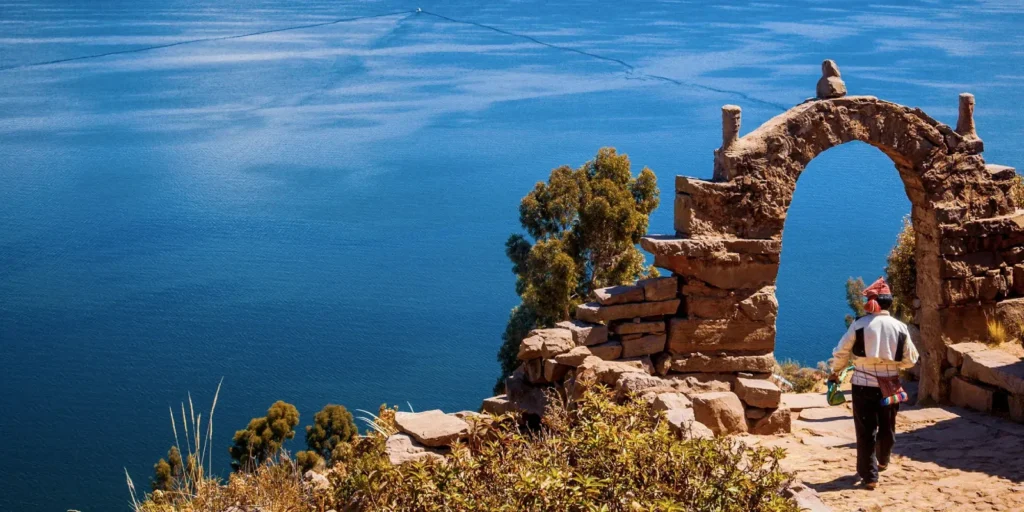 Persona camina bajo arco de piedra con vista al lago Titicaca en Taquile