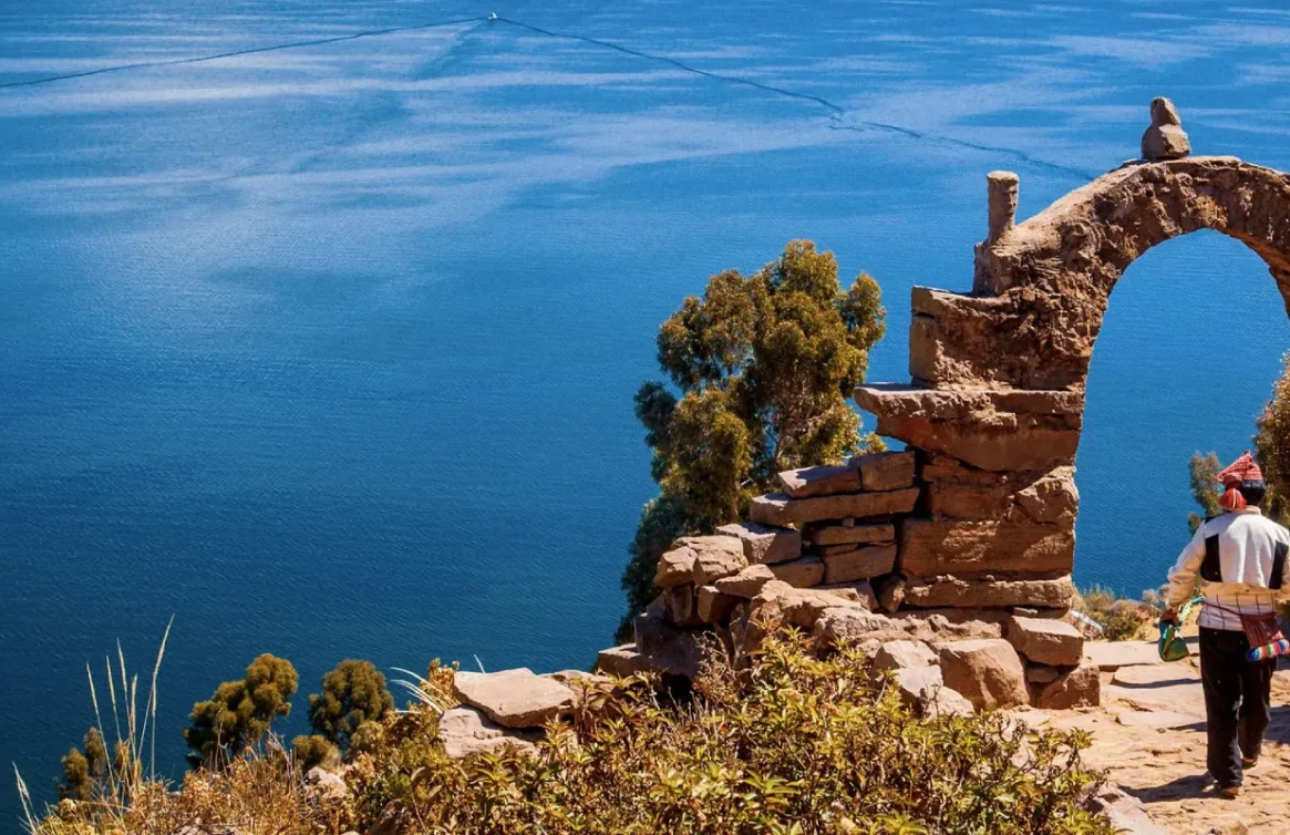 Uma pessoa caminha sob um arco de pedra com vista para o Lago Titicaca em Taquile.