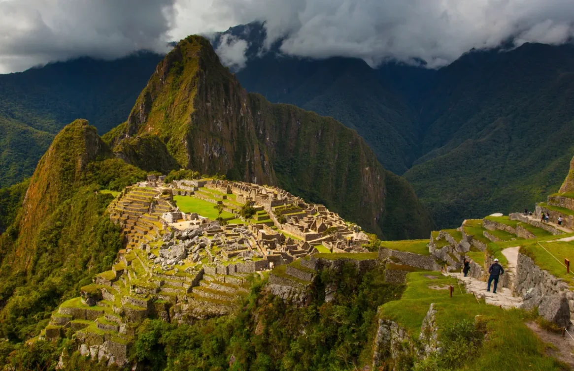 Vista panorâmica de Machu Picchu cercada por montanhas verdes sob um céu nublado.
