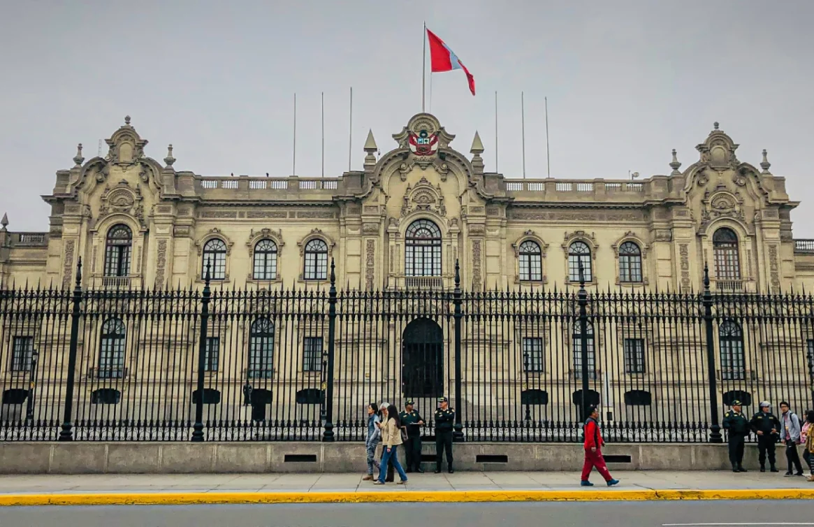 Palacio de Gobierno del Perú, con bandera ondeando y personas caminando frente a él