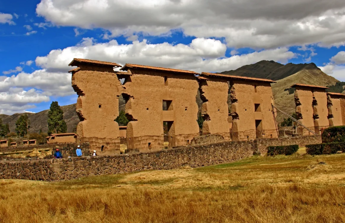 Ruínas do templo Raqchi com montanhas ao fundo e céu nublado.