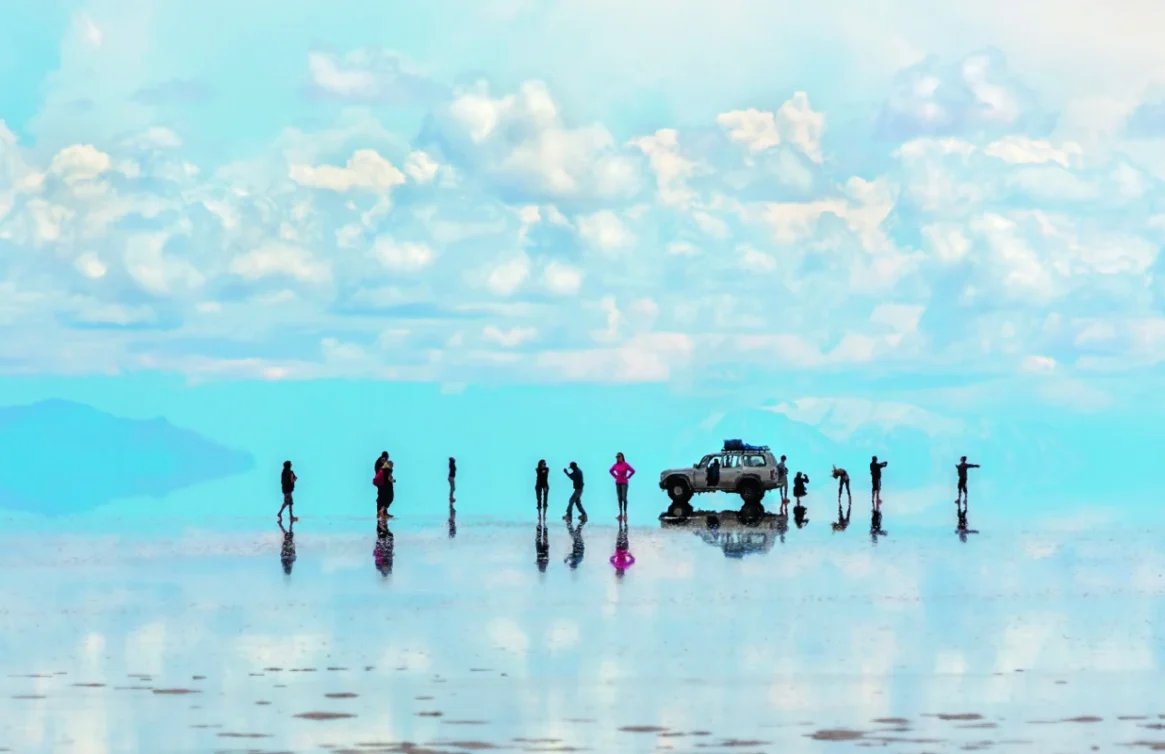 Pessoas e carros refletidos nas águas do Salar de Uyuni, Bolívia.