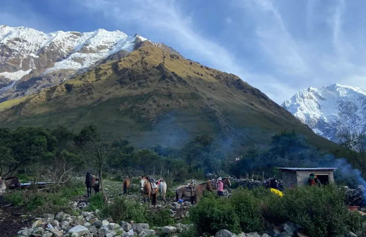 Cavalos e pessoas acampando no sopé das montanhas cobertas de neve na Trilha Salkantay, Peru.