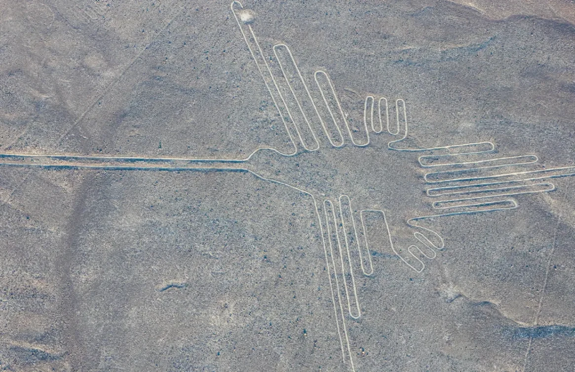 Línea de Nazca con figura de colibrí en un desierto rocoso, colinas al fondo.