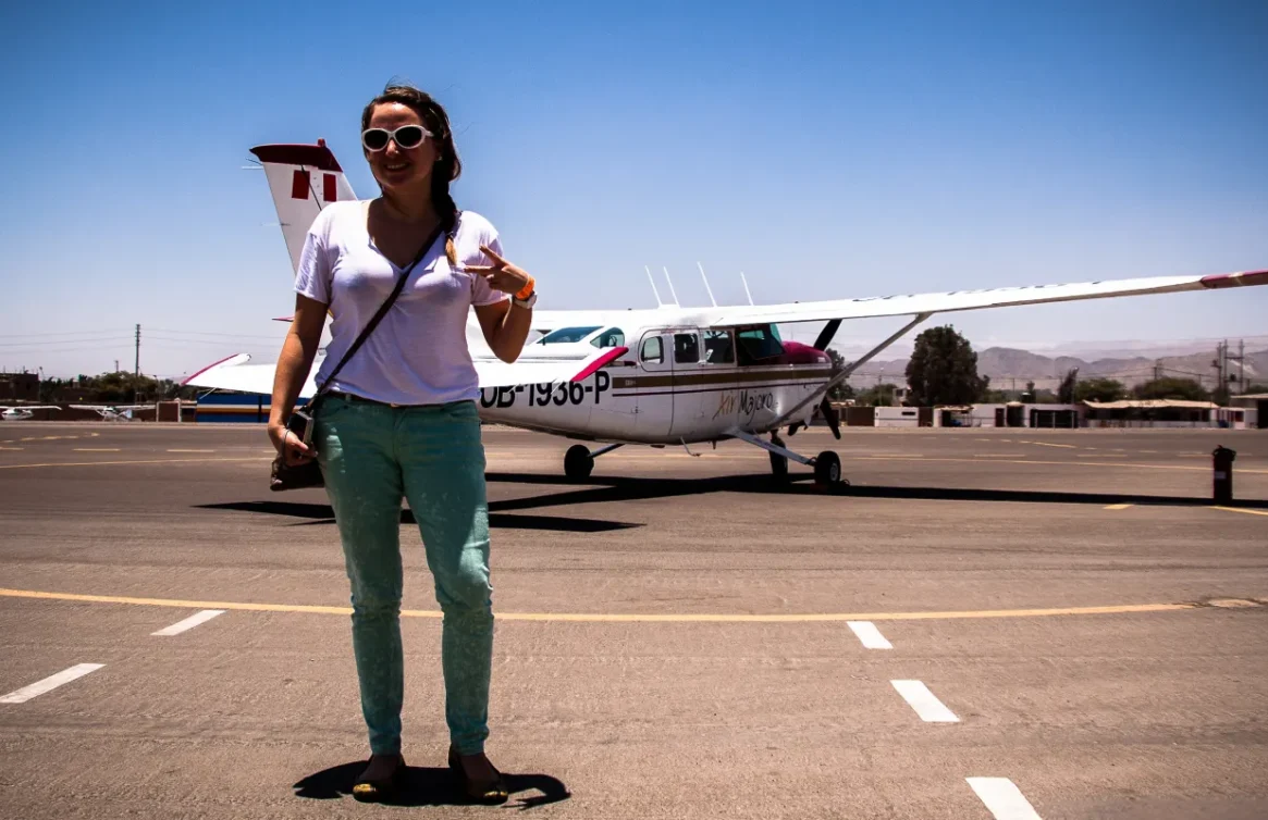 Turista en pista de aterrizaje en Nazca con avioneta "Air Majoro" al fondo, cielo despejado y montañas lejanas.