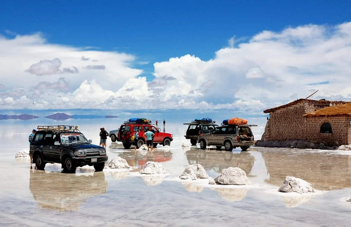 Jipes e turistas no Salar de Uyuni ao lado de uma construção rústica.